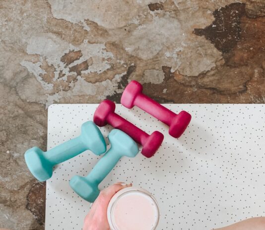 필라테스와 식단: “단백질 쉐이크가 답일까?” 효과를 200% 만드는 영양학 가이드 person holding white liquid filled cup above two pairs of dumbbells